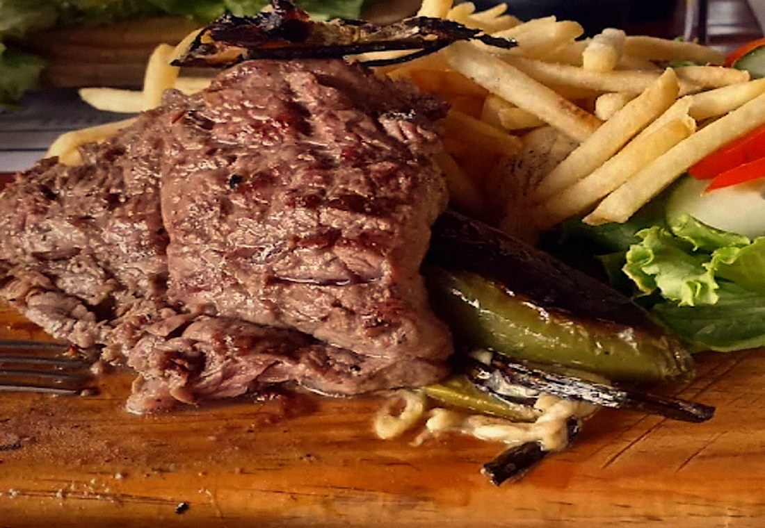 Corte de arrachera recién asado, servido en tabla de madera con papas, ensalada y chiles toreados