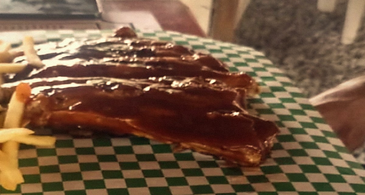 Costillas BBQ glaseadas sobre papel a cuadros verde, acompañadas de papas a la francesa